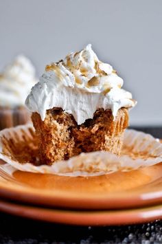 two cupcakes with white frosting sitting on top of a brown and orange plate