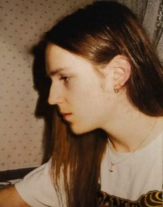 a woman with long hair is looking at something in the distance while wearing a white t - shirt