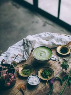 two cups filled with green liquid sitting on top of a wooden table next to flowers