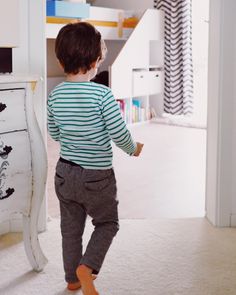 a little boy standing in front of a white dresser