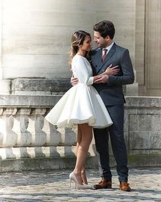 a man and woman standing next to each other in front of a white building with columns