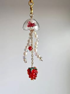 a red apple hanging from a chain on a white background with beads and chains attached to it