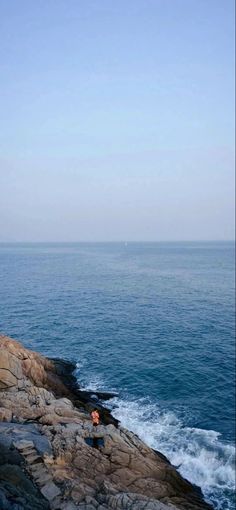 two people are sitting on the rocks near the ocean and looking out at the water