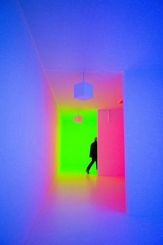 a person walking through a brightly lit room with neon colors on the walls and ceiling