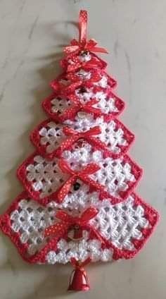 a crocheted christmas tree ornament hanging on a wall with a bell