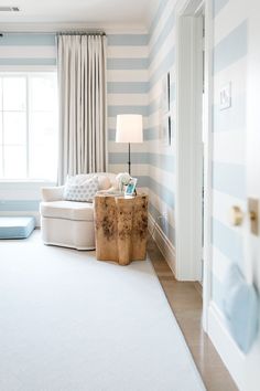 a living room with blue and white stripes on the walls, carpeted flooring and furniture