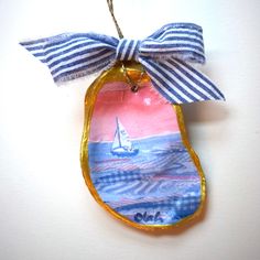 an ornament with a sailboat on the water and a blue ribbon hanging from it