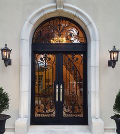 the front entrance to a house with two potted plants on either side and an ornate iron door