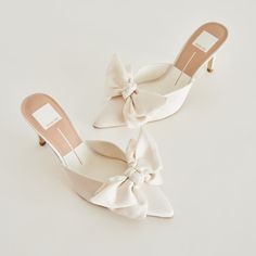 two pairs of white shoes with bows on the heel and heels in the front, one is