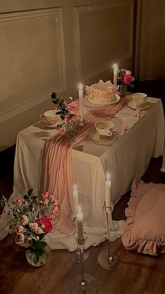 the table is set with candles, plates and pink napkins on top of it