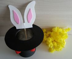 a paper bunny mask next to a cup with yellow flowers in the foreground and a black hat on top