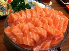 a bowl filled with raw salmon on top of a wooden table next to other food