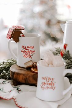 two coffee mugs sitting on top of a wooden table next to a christmas tree