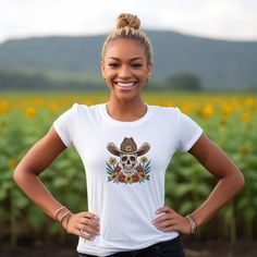 Saddle up and get ready to ride in our Cowboy Skull and Wildflowers Unisex Tee. This jersey short sleeve tee features a striking cowboy skull surrounded by vibrant wildflowers, paying homage to folk art design. Perfect for any cowgirl or cowboy, this tee seamlessly combines unique style with comfort, making it a must-have addition to your wardrobe. Giddy up and add a touch of Western flair to your look today. #15 Folk Art Classic unisex jersey short sleeve tee fits like a well-loved favorite. So Day Of The Dead Skull Print T-shirt, Day Of The Dead Skull Print Short Sleeve T-shirt, Day Of The Dead Skull Print Short Sleeve Tops, Fitted T-shirt With Skull Graphic Print, Cowboy Skull, Folk Art Design, The Wild West, Arte Popular, Prism Color