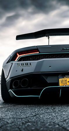 the rear end of a black sports car with its hood up and lights on, in front of a cloudy sky