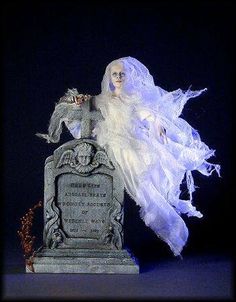 a statue of a woman with white hair and veil on it's head sitting in front of a grave