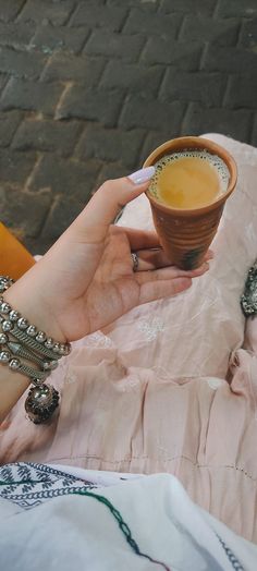 a woman holding a cup of coffee on top of a pink cloth covered tablecloth