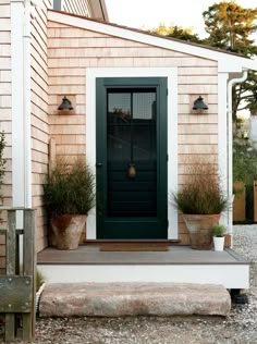 a green door is on the side of a house with potted plants in front