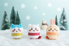 three small stuffed animals sitting on top of snow covered ground with trees in the background