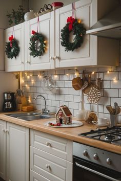 a kitchen decorated for christmas with wreaths on the wall and lights hanging from the cabinets