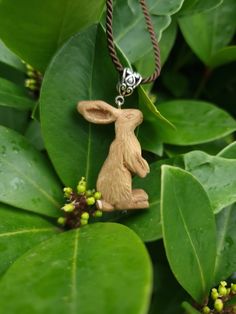 a small wooden rabbit sitting on top of a green leafy plant with beads in its mouth