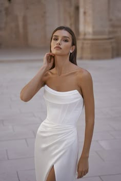 a woman in a white dress posing for the camera with her hand on her cheek