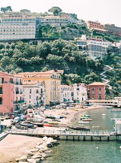 the beach is lined with boats and houses on top of a hill in the background