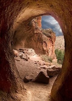 a cave entrance in the desert with rocks and trees on both sides, under a cloudy sky