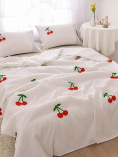 a bed covered in white sheets with cherries on them and two pillow cases sitting next to each other