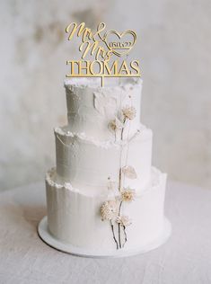 a three tiered white cake with flowers on the top and bottom, sitting on a table