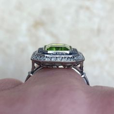 a close up of a person's hand holding a ring with a green stone in it