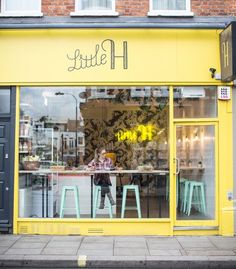 a person sitting at a table in front of a yellow storefront with flowers on it