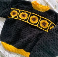 a knitted sweater with sunflowers is laying on a bed next to a pillow