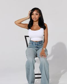 a woman sitting on top of a chair wearing high waist jeans and a white tank top