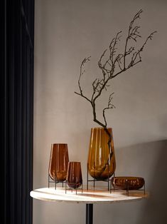 three vases are sitting on a table in front of a wall with a tree branch