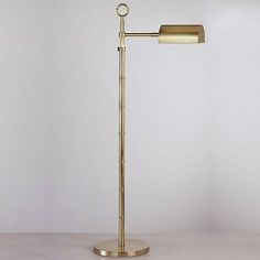 a gold floor lamp on a white surface with a round light fixture in the middle