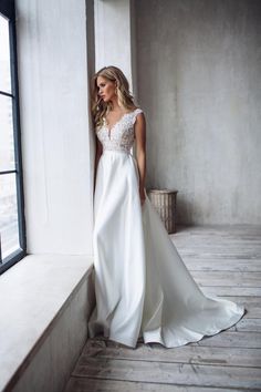 a woman standing in front of a window wearing a white dress