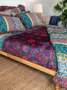 a bed with colorful bedspread and pillows on top of it next to a potted plant