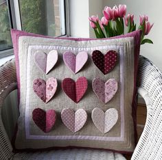 a pillow made out of hearts sitting on a chair next to a vase with tulips