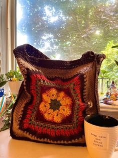 a crocheted bag sitting on top of a table next to a mug and window