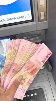 a person holding money in front of an atm machine