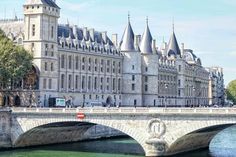 a bridge over water in front of a large building with turrets on it's roof