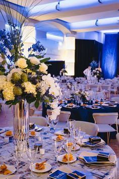 a table set up for a formal function with blue and white flowers in a tall vase