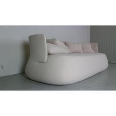 a large white couch sitting on top of a floor next to a wall with two pillows