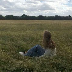 a woman sitting in the middle of a field with a kite flying over her head