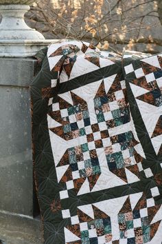 a black and white quilt sitting on top of a stone wall next to a tree