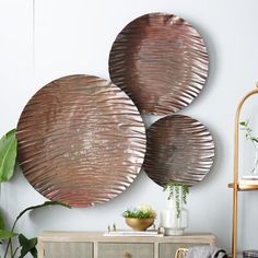 three circular metal wall hangings on a white wall next to a dresser and potted plant