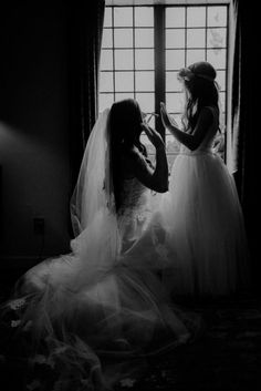 two women in wedding gowns standing by a window