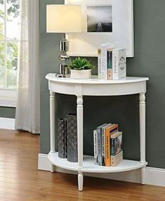 a small white table with a mirror and lamp on it's side shelf next to a window