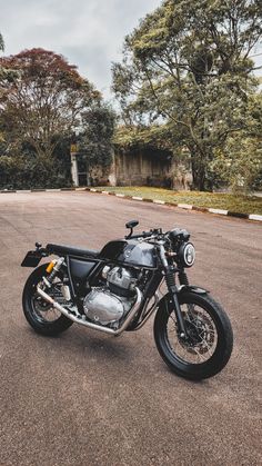 a black motorcycle parked in the middle of a parking lot next to trees and bushes